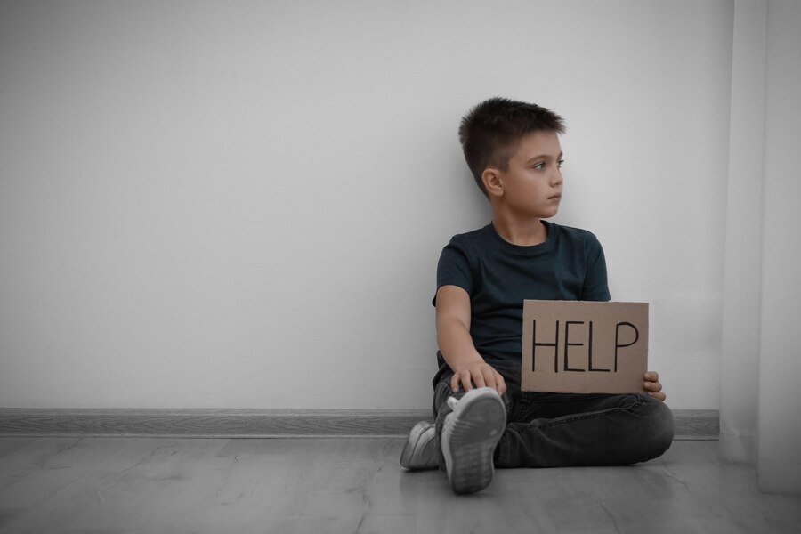 Sad little boy with sign HELP sitting on floor indoors space for text Child in danger