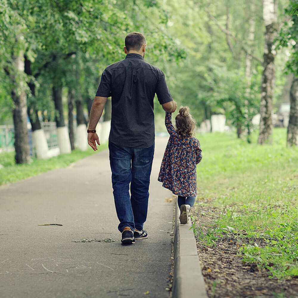 Man and child holding hands on tree-lined path, coping with depression and single parenting in NYC.