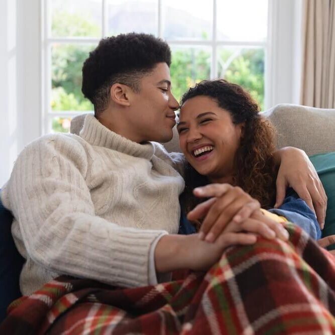 Happy couple sitting on couch under blanket, laughing