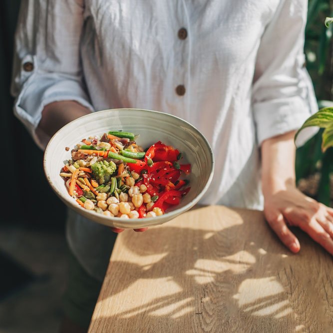 Young woman eating healthy food sitting in beautiful interior with green flowers on the background