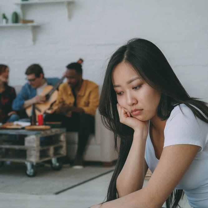 Young asian girl feels upset and isolated while her flatmates celebrating party at home