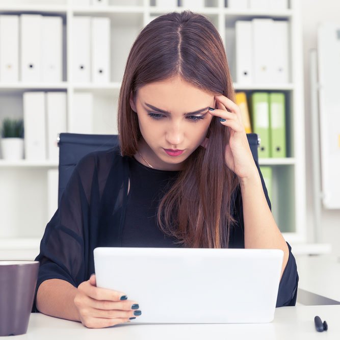 Serious girl in black is looking at her tablet computer screen.