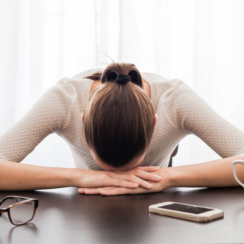 Woman resting head on crossed arms at desk, dealing with PCOS fatigue in NYC.