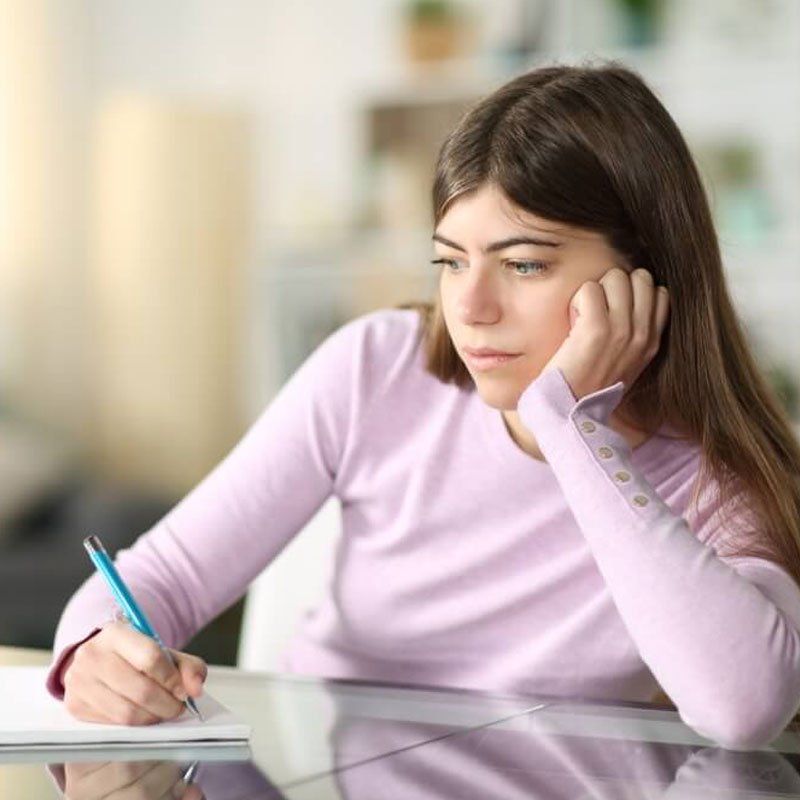 Person in a pink shirt writing at a desk, highlighting ADHD signs in high-achieving women in NYC.