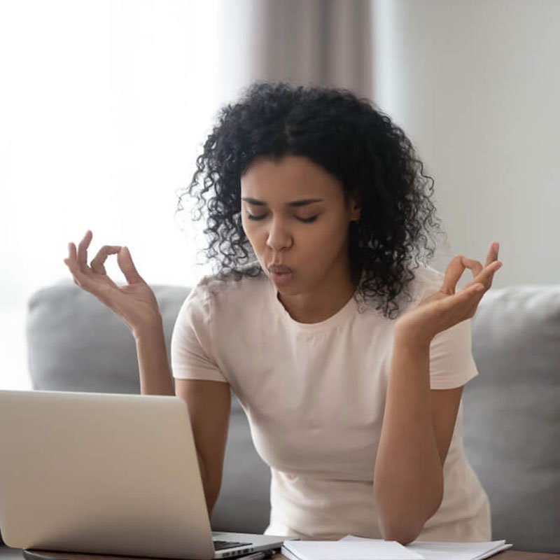 Woman in a white shirt meditating at a desk with a laptop and papers, addressing anxiety in NYC.