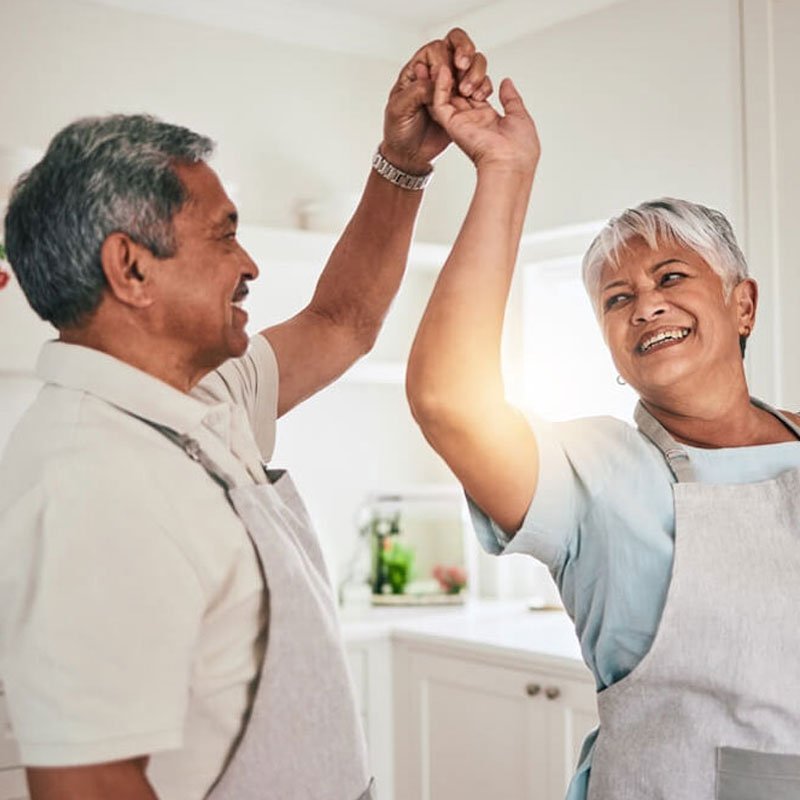 Two seniors dancing joyfully in a kitchen, discussing emotional entanglement in NYC.