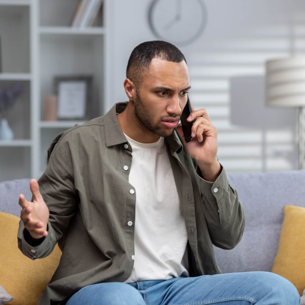 Person in a casual shirt sitting on a sofa, coping with phone call anxiety in NYC.