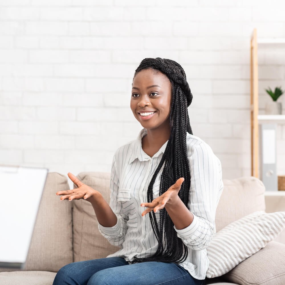 Person with braids gesturing while sitting on a couch, exploring millennial therapy in NYC.