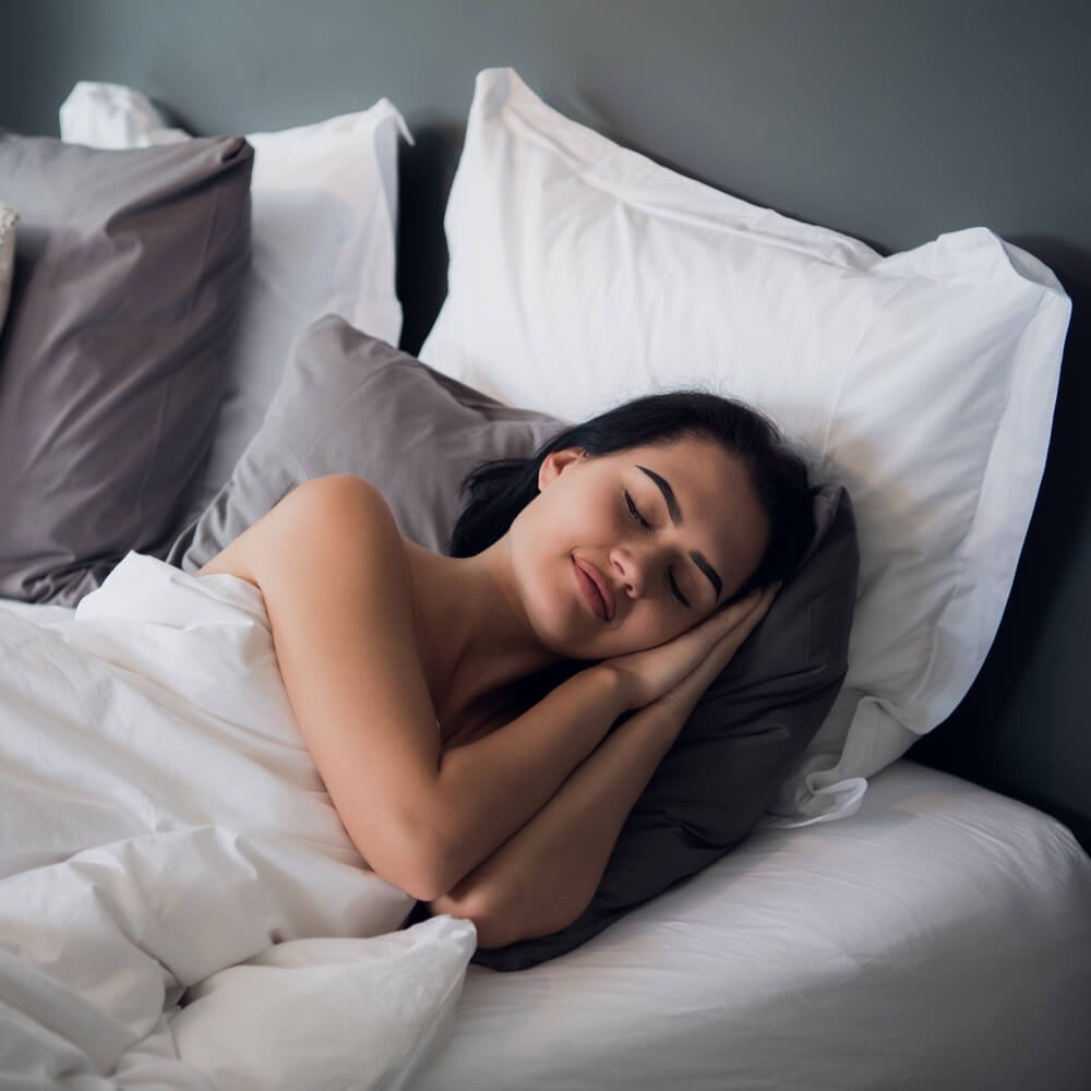 Person curled up in bed with white and grey pillows, focusing on better sleep through CBT in NYC.