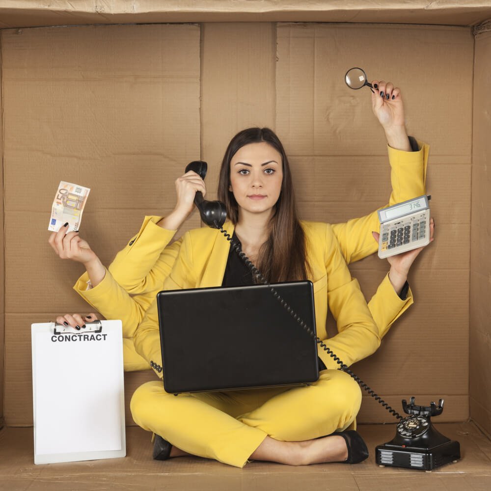 Multi-tasking person in yellow suit with phone, laptop, calculator, exploring workaholism in NYC.
