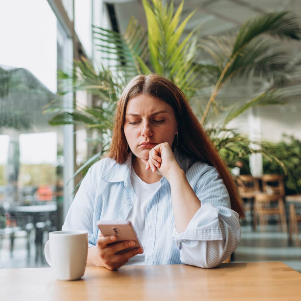 Person in a striped shirt holding a phone at a table, navigating dating with anxiety in NYC.