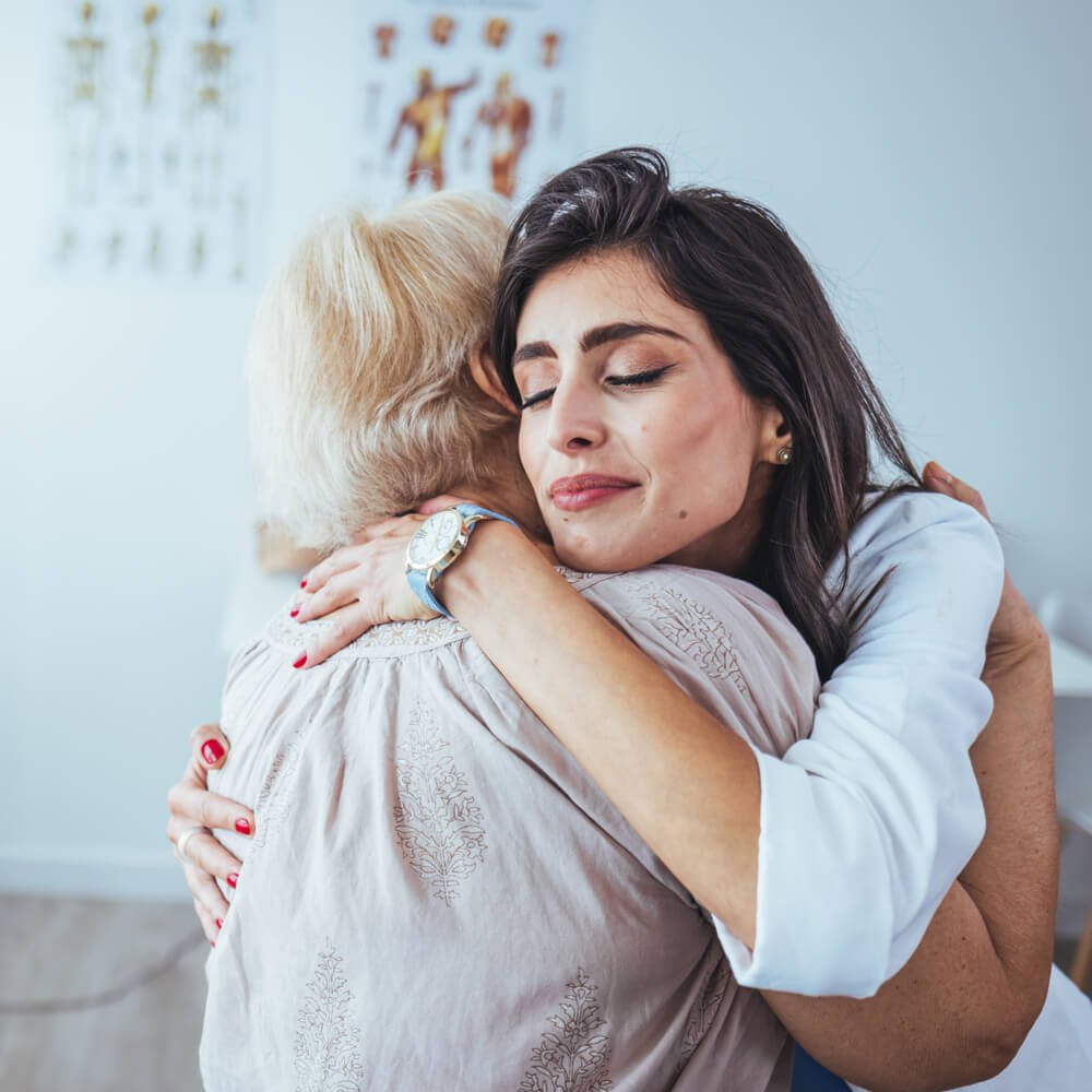 Two women hugging with a medical poster in the background, exploring empathy vs. sympathy in NYC.