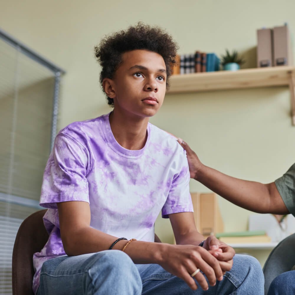 Person in a tie-dye shirt with supportive hand on their shoulder, focusing on Gen Z therapy in NYC.