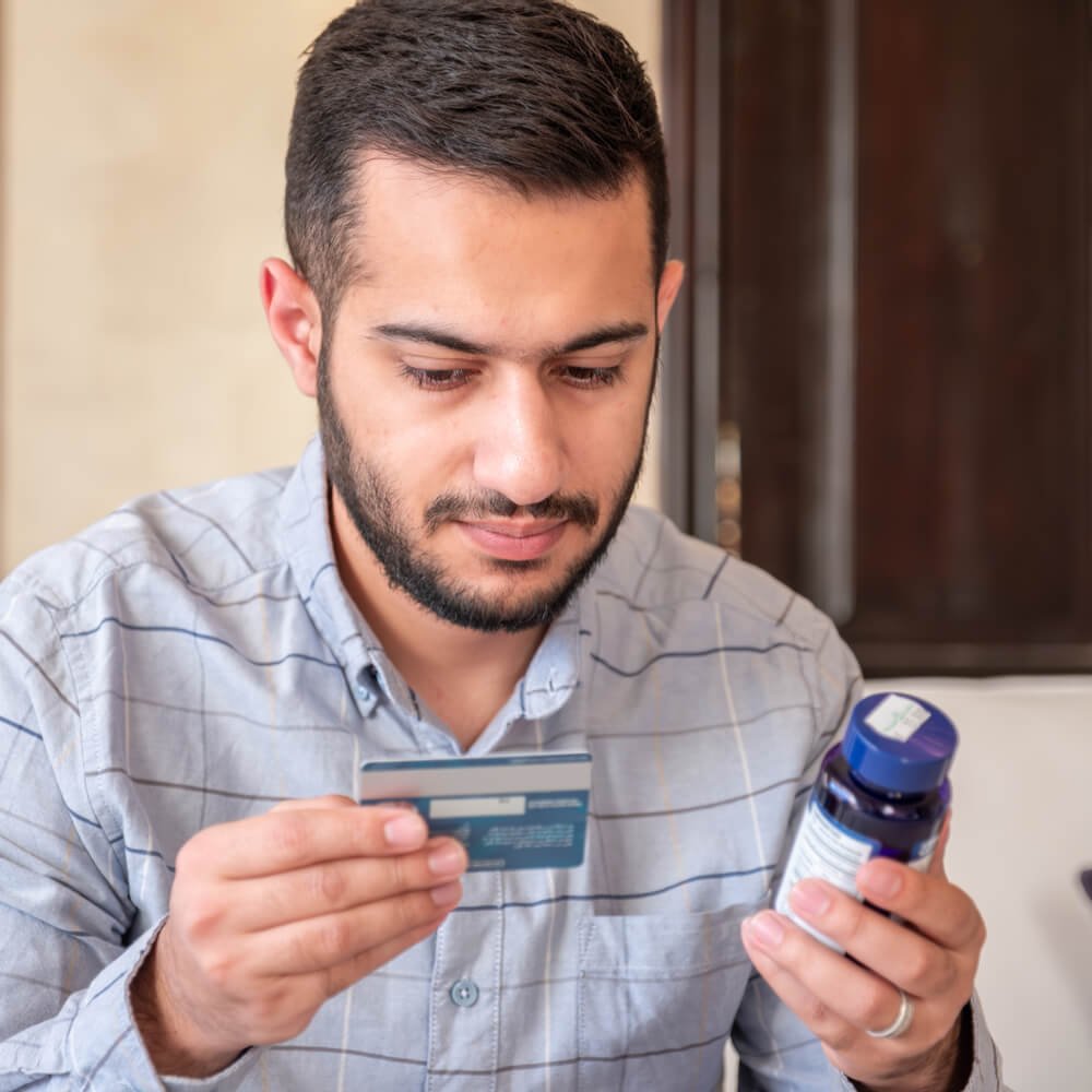 Person holding a credit card and medicine bottle, illustrating therapy costs in NYC.