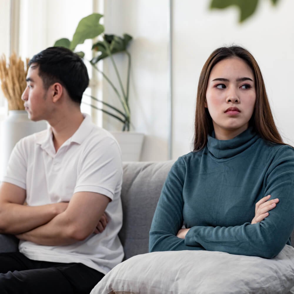 Two people sitting on a sofa with crossed arms, reflecting an unhappy marriage in NYC.