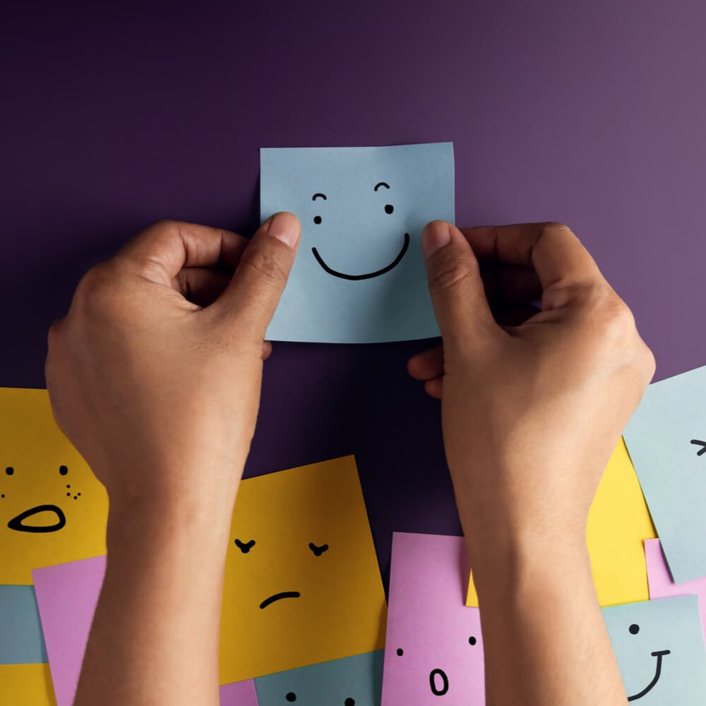 Hands holding sticky note w/ a smiley face, emphasizing gratitude's impact on mental health in NYC.