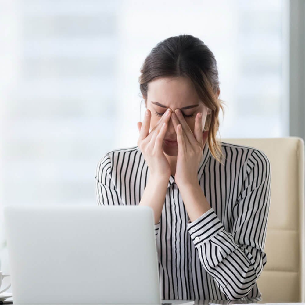 Woman in striped shirt using a laptop at a desk, exploring stress and hormonal imbalance in NYC.