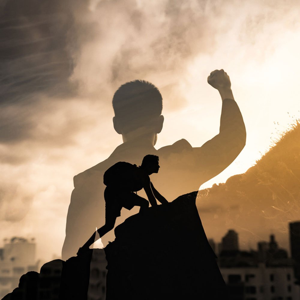 Silhouette climbing a hill with a raised fist, highlighting motivation vs. inspiration in NYC.