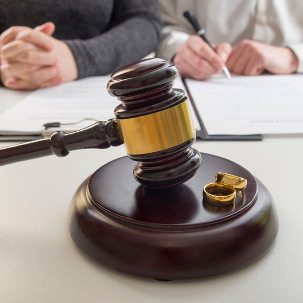 Gavel and wedding rings on a table with two people, reflecting divorce proceedings in NYC.