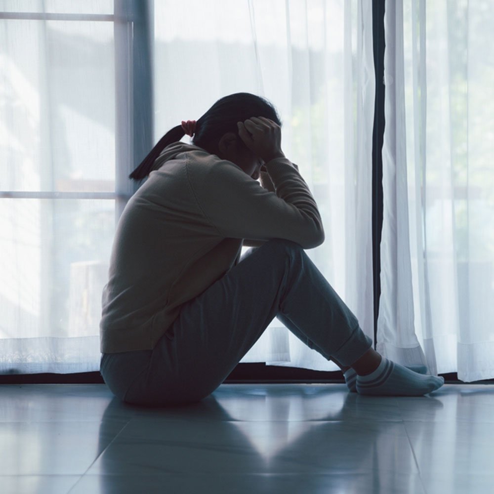 Person sitting on the floor by a window, coping with bipolar anger in NYC - Uncover Counseling.