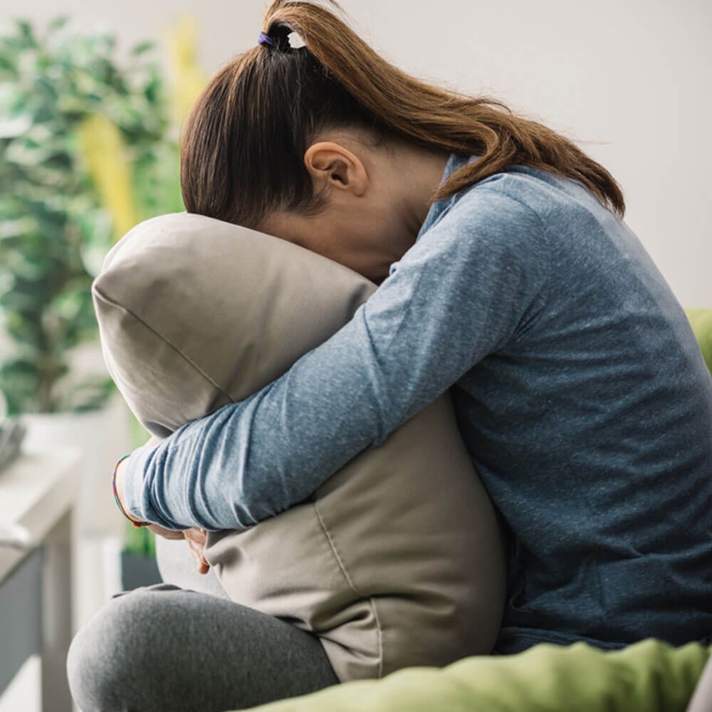 Person hugging knees on a green couch, managing negative emotions in NYC.