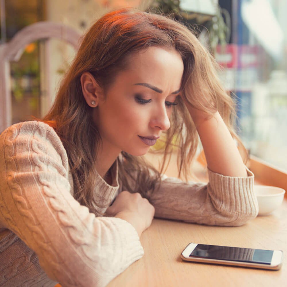 Person resting head on hand at table with smartphone, overcoming fear of being alone in NYC.