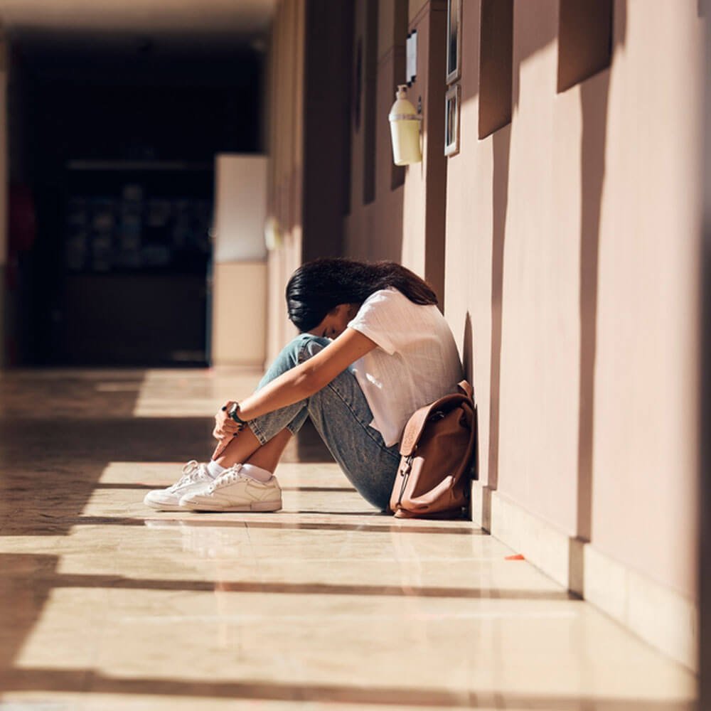 Person sitting on the floor, head down, facing bullying effects in NYC.