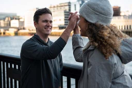 Two people giving a high five by a waterfront railing with the cityscape.