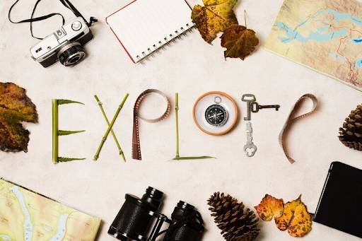 Flat lay of travel items with "EXPLORE" spelled out, camera, compass, binoculars, map, etc.