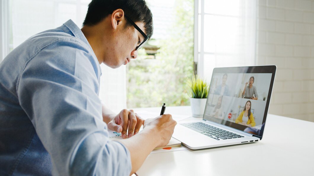 teletherapy - a young man writing on his notebook while doing a meeting